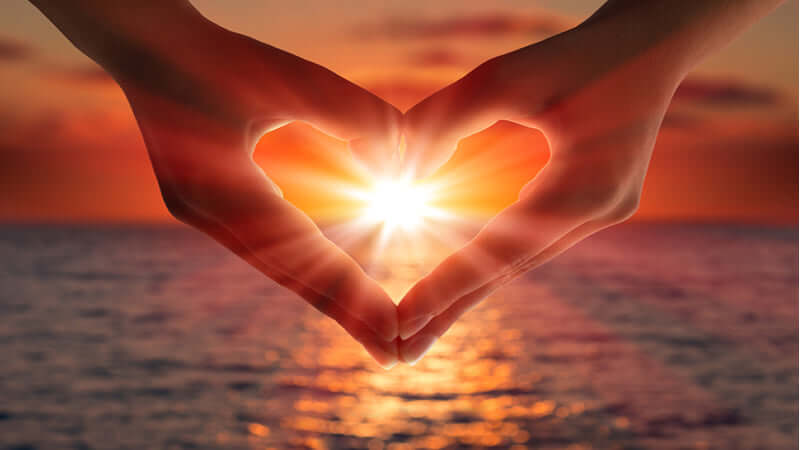 Hands forming a heart shape with the sun shining, representing Love and Light in a serene sunset.