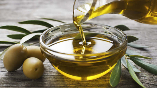 Pouring olive oil into a bowl surrounded by olives, representing healthy fats in the context of Interviewing Mary Enig on Health Risks from Trans Fats.