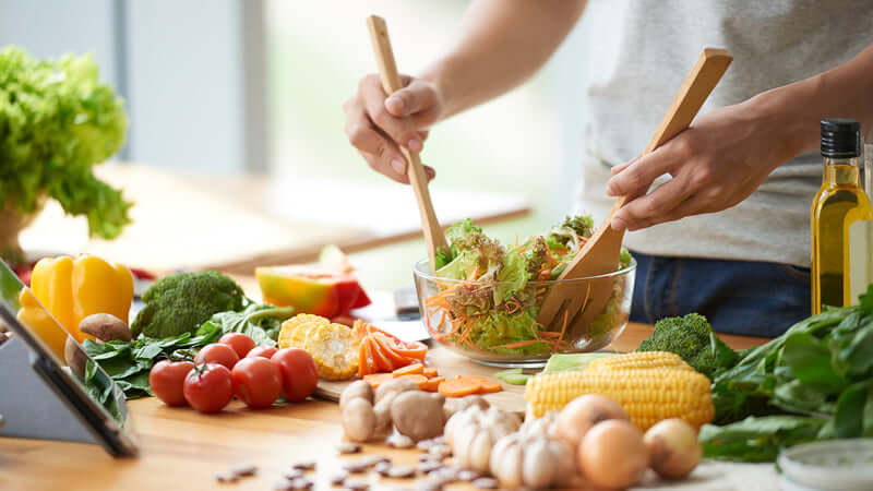 Argument for Meatless Diet: Fresh vegetables and greens being mixed in a bowl in a modern kitchen