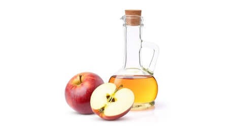 A bottle of Apple Cider Vinegar next to a whole apple and a sliced apple.