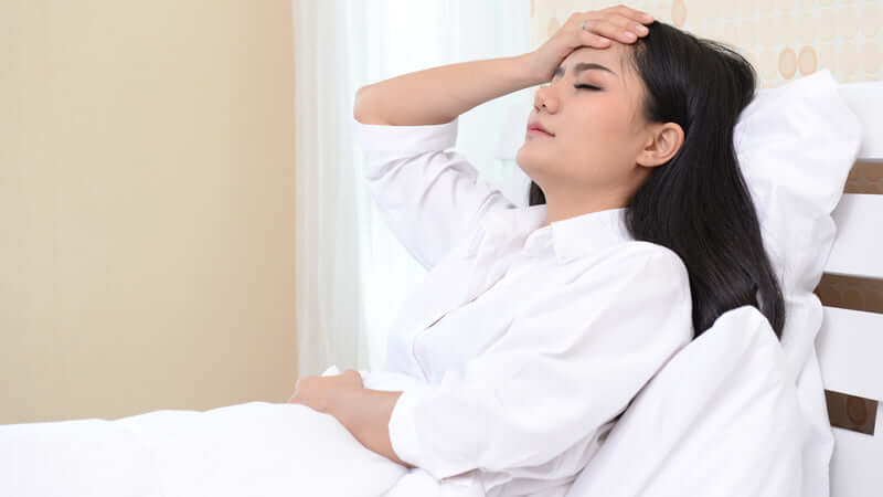Woman resting in bed with a headache, exploring Adaptogenic Herbs and How They Work for relief.
