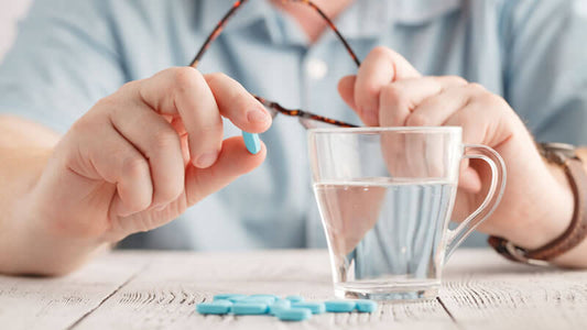 Person holding a blue pill over a glass of water, representing drugs contaminating water.
