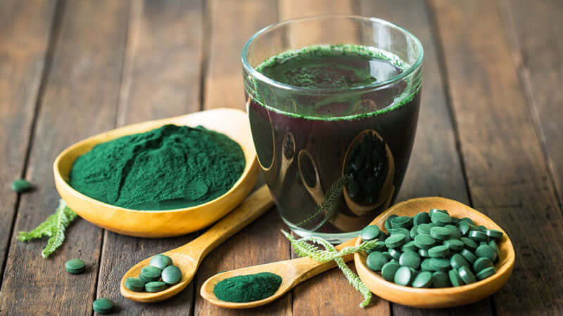 AFA Benefits: Green powder and drink made from spirulina, including pills and powder on wooden table.
