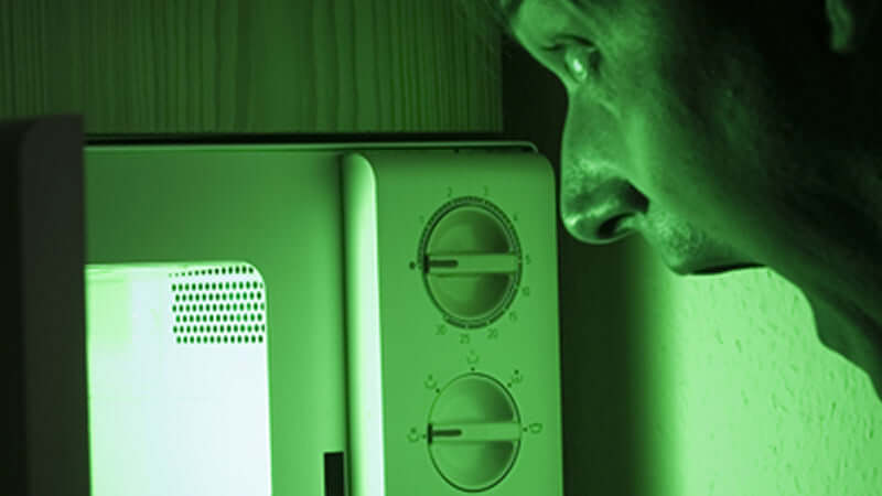Person looking anxiously at a microwave, illustrating concerns about Microwaved Food Harmful Effects.
