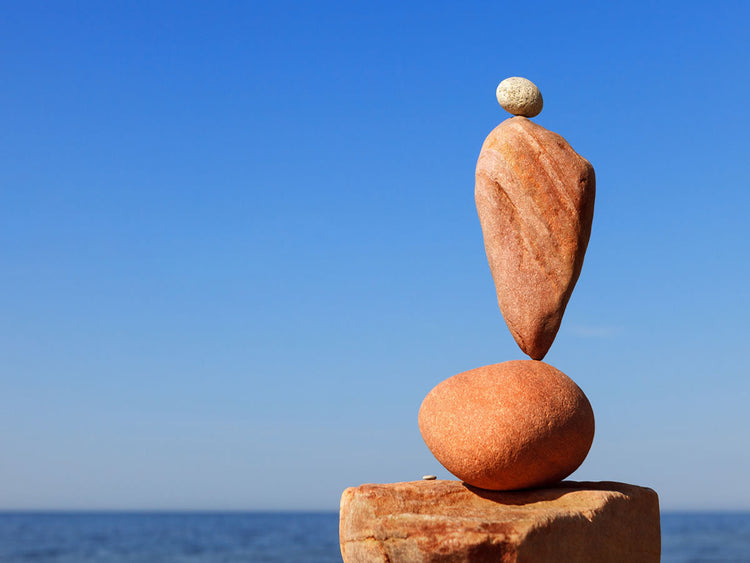 Balanced stones stacked on a beach against a clear blue sky, symbolizing harmony and stability.