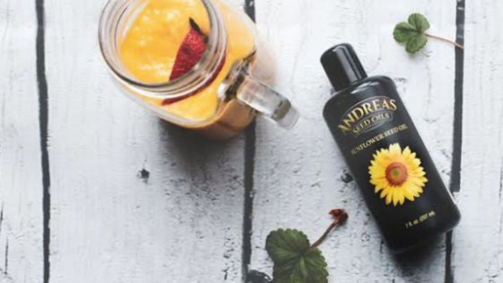 Cold Pressed Sunflower Oil bottle next to a smoothie in a mason jar on a wooden surface.