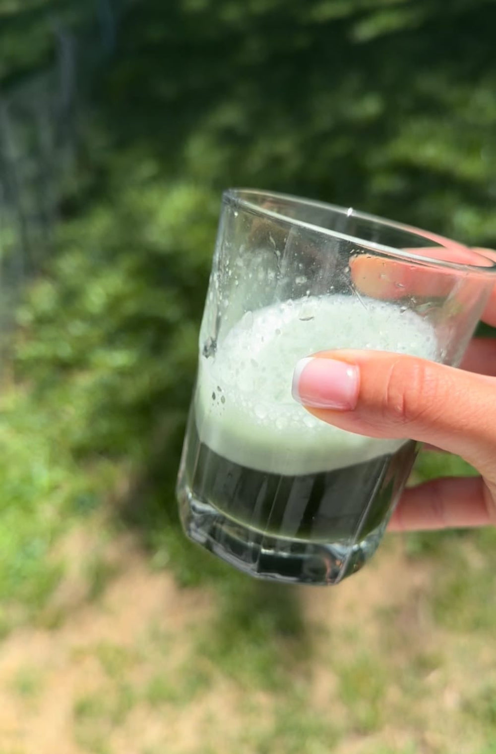 Cyanobacteria Phycocyanin and Chlorophyll Synergy Support drink held outdoors in a glass, showcasing vibrant green color.