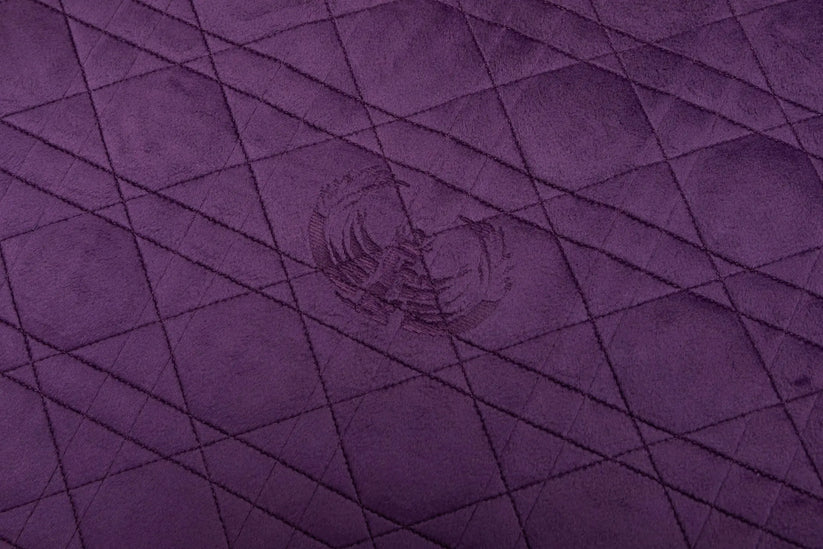 A close-up of a purple quilted fabric with a diamond pattern and a subtle central logo.
